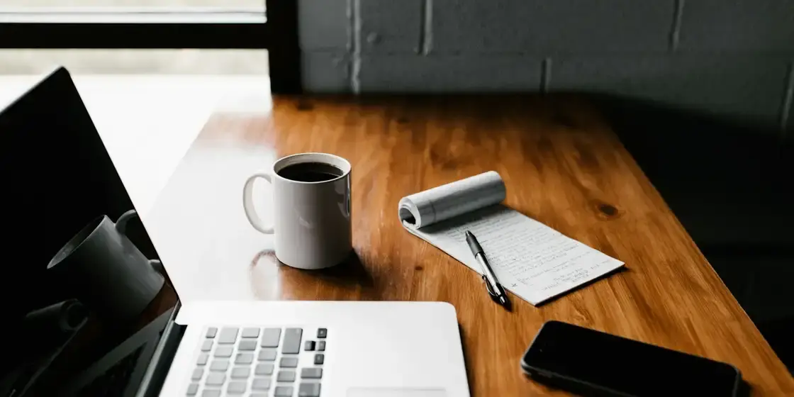 Escritorio de madera con un portátil abierto, una libreta y una taza de café